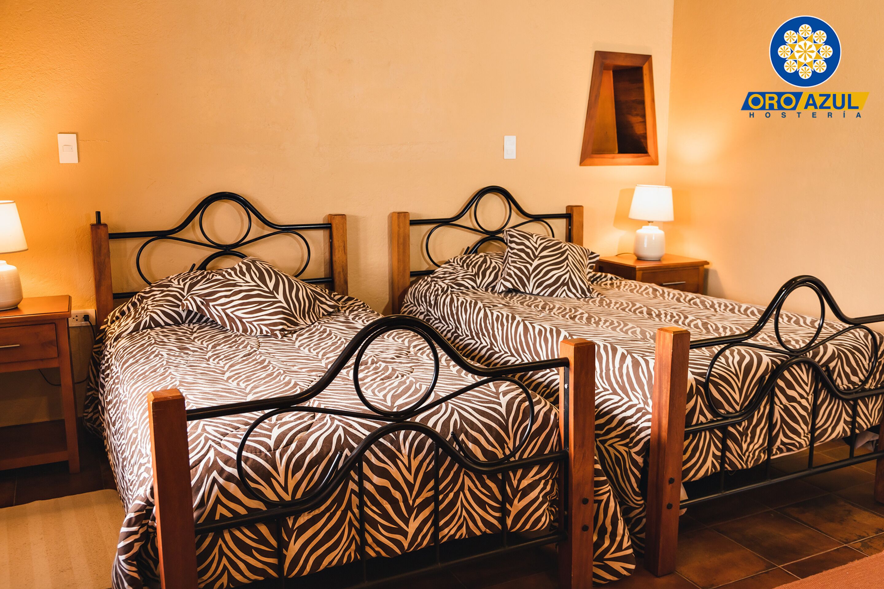 A room with two beds, each with a zebra-patterned bedspread, wooden headboards, and bedside tables with lamps.