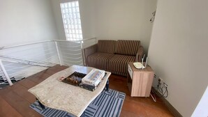 A living room with a sofa, a coffee table with board games, a small side table with a router, and a window with blinds. - Casa do Bert Itanhaén (Itanhaém)