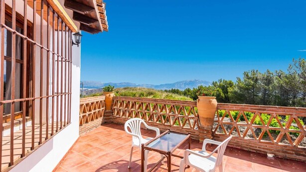 Une terrasse avec une table et des chaises, un pot de fleurs et une vue sur les montagnes.