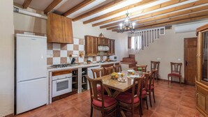 Une cuisine avec un coin repas, des poutres apparentes en bois au plafond, un lustre et un pare-feu en carrelage.