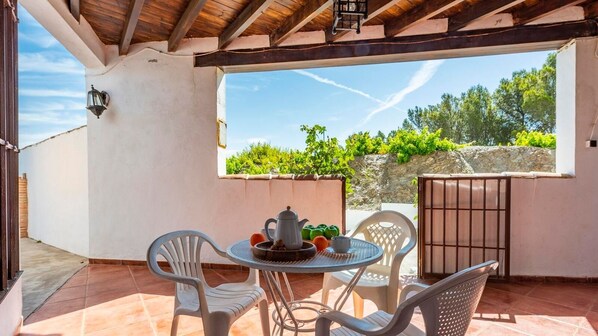 Une terrasse couverte avec une table et des chaises, une vue sur la verdure et un mur en pierre.