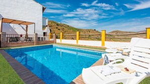 Une piscine avec vue sur les collines, un patio couvert avec des meubles d’extérieur et un bâtiment blanc.