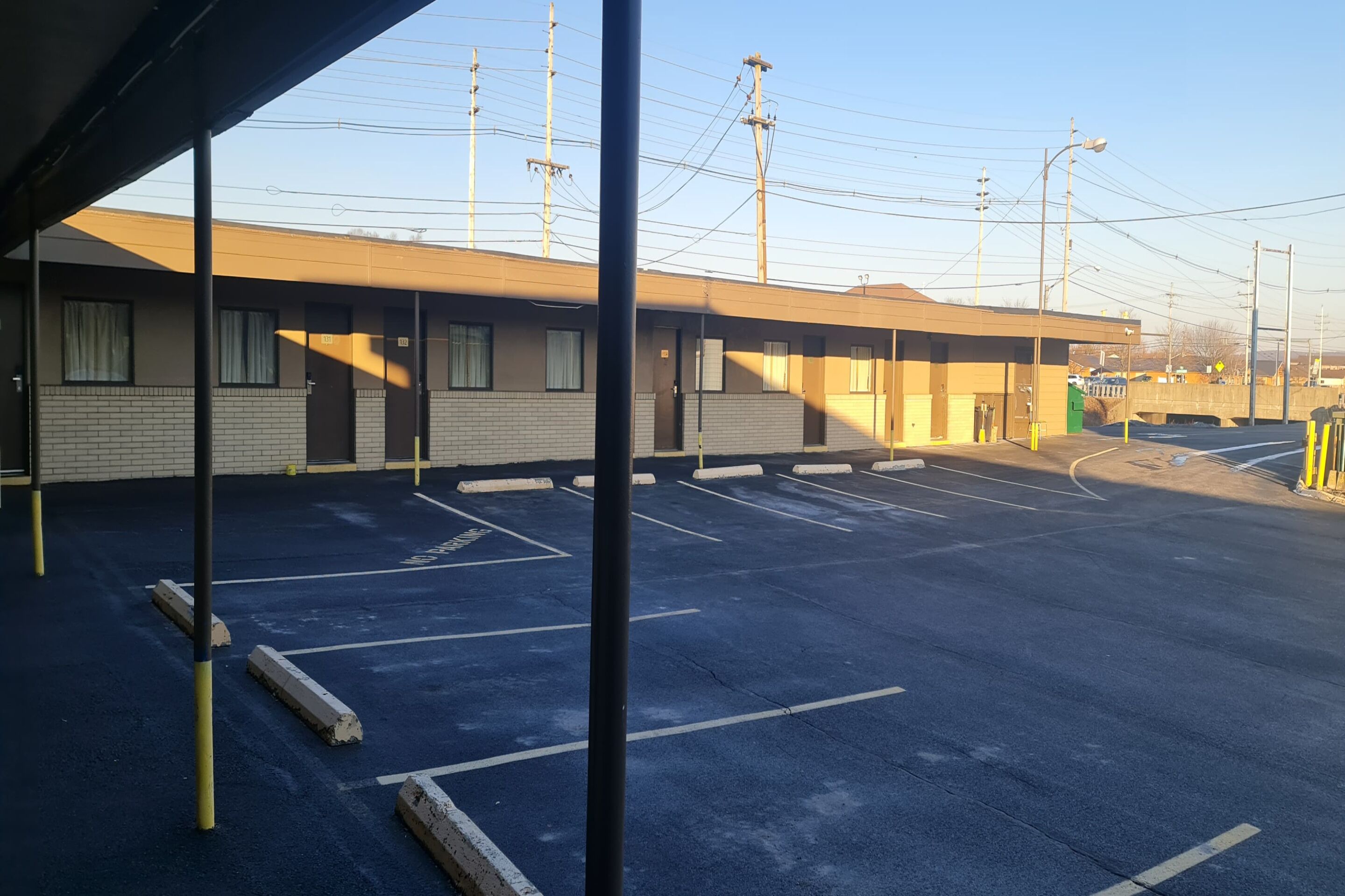 Un motel con estacionamiento, una zona techada y un edificio con varias habitaciones.