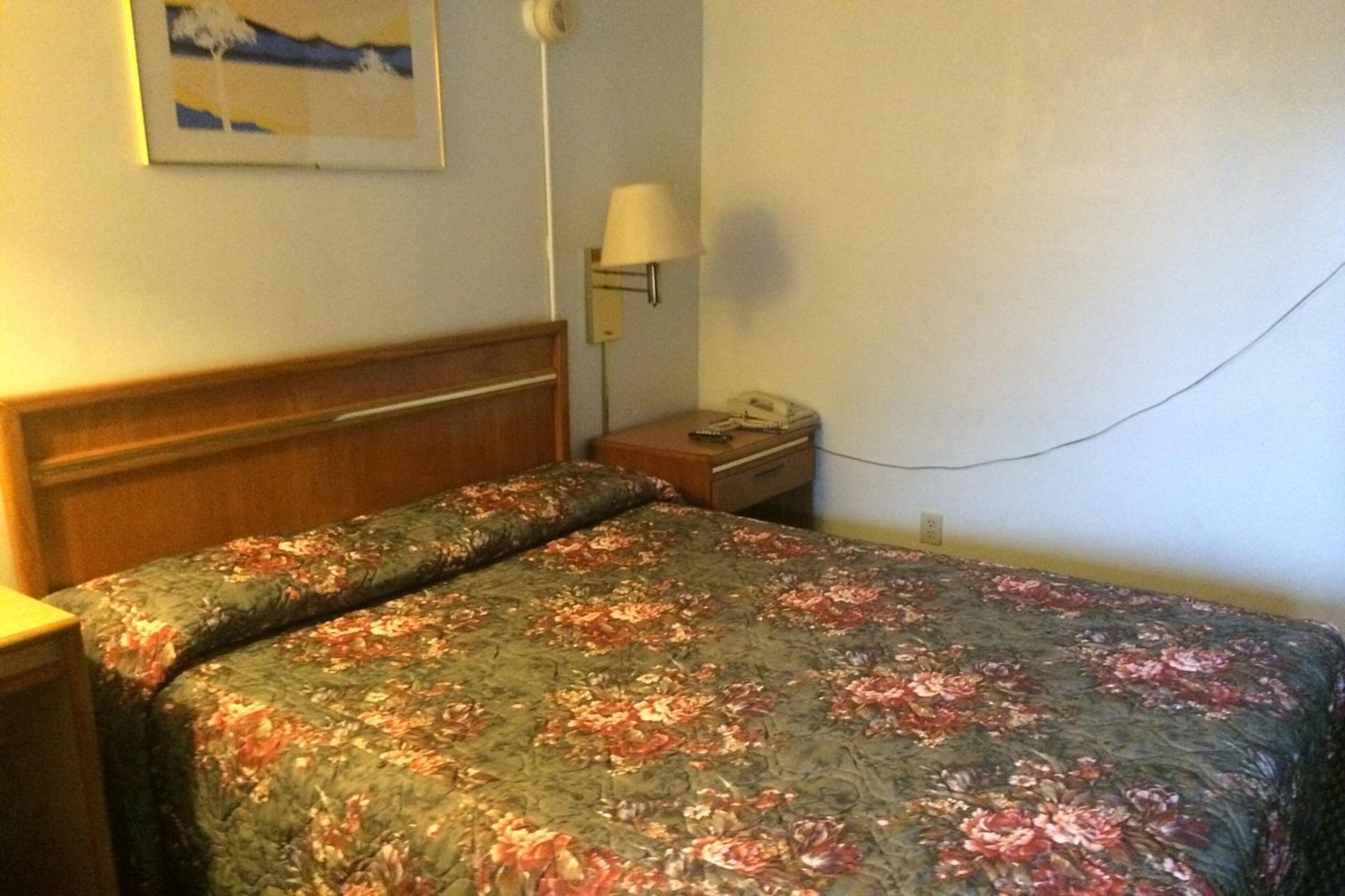 A hotel room with a bed, a nightstand, a lamp, and a telephone.