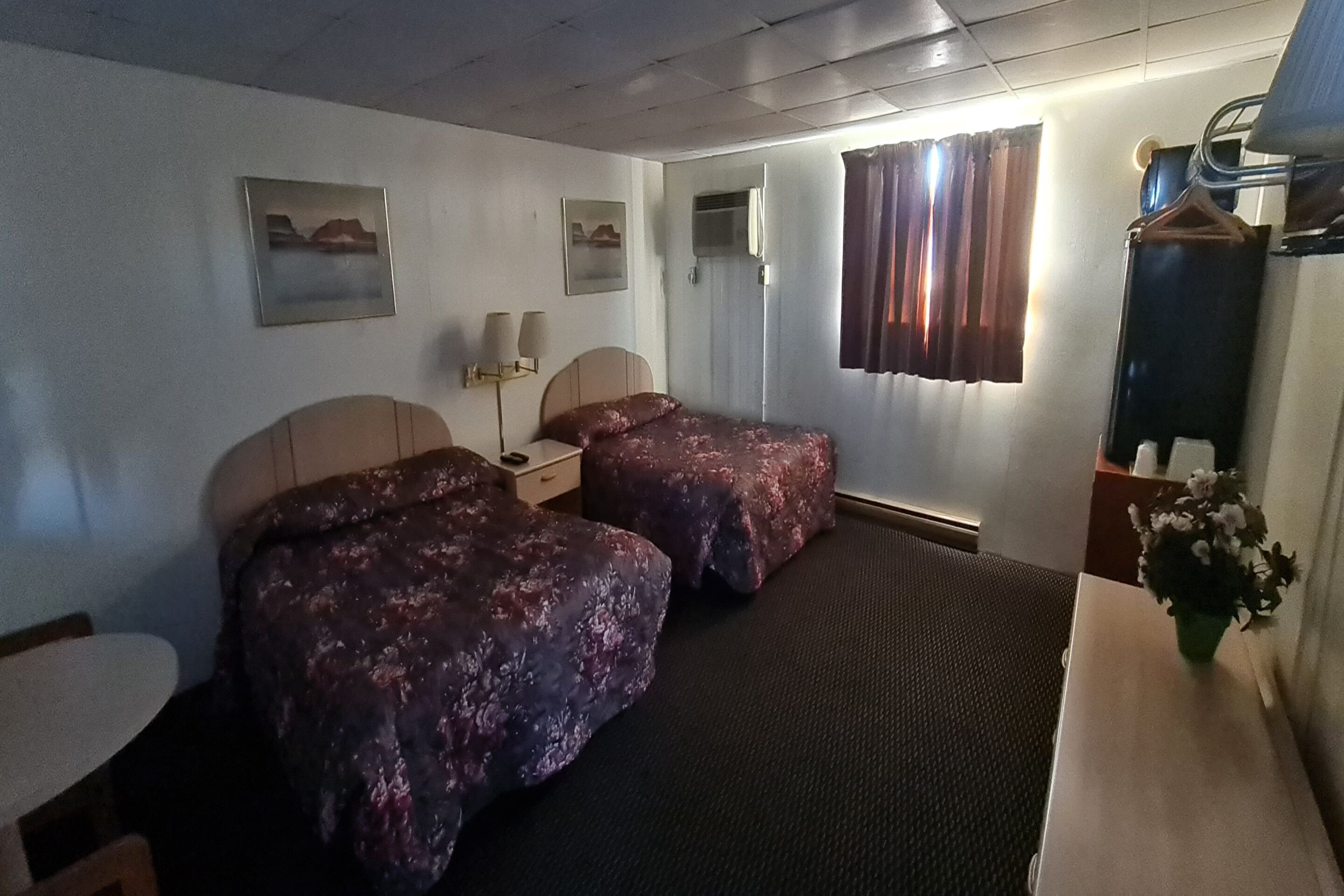 Ein Hotelzimmer mit zwei Betten, einem Schreibtisch, einem Sessel, einem Schminktisch und einem Fenster mit Vorhängen.