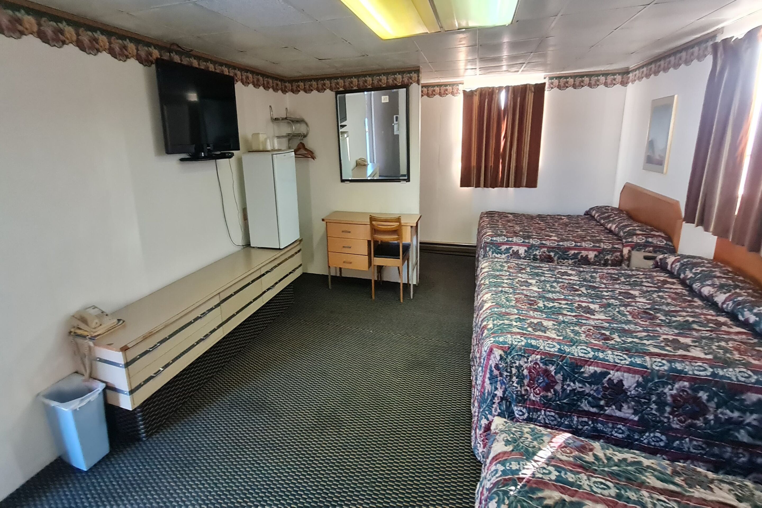 Une chambre comprenant un lit, un bureau, une chaise, un miroir, une télévision et une armoire.