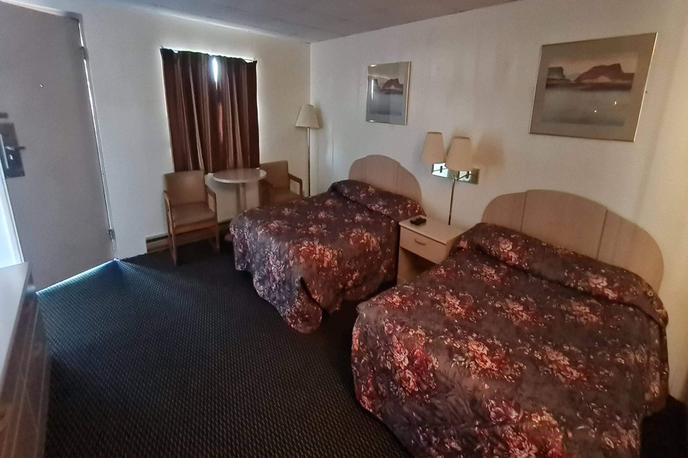 A hotel room with two beds, a desk, a chair, a lamp, and a window with curtains.