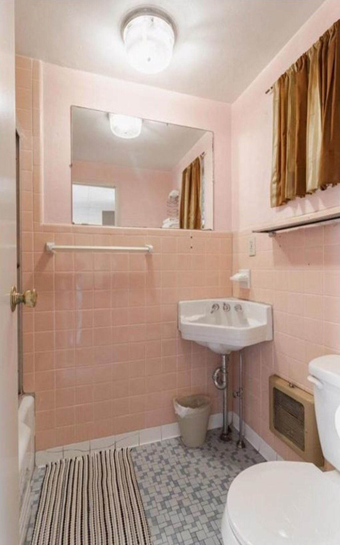 Un baño con azulejos rosas, un lavabo blanco, un espejo, una ducha y un felpudo a rayas.