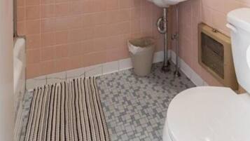 Un baño con azulejos rosas, un lavabo blanco, un espejo, una ducha y un felpudo a rayas.