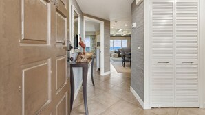 A hallway with a brown door, a white closet, and a view to a living area with a couch and a window. - Spectacular Ocean Front Condo on the Omni Plantation (Fernandina Beach)