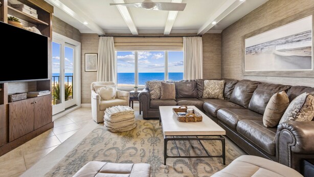 A spacious living room with a large leather sofa, a flat-screen TV, and a view of the ocean through large windows. - Spectacular Ocean Front Condo on the Omni Plantation (Fernandina Beach)