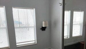 A room with two windows, a wall-mounted lamp, a large mirror, and a wooden dresser.