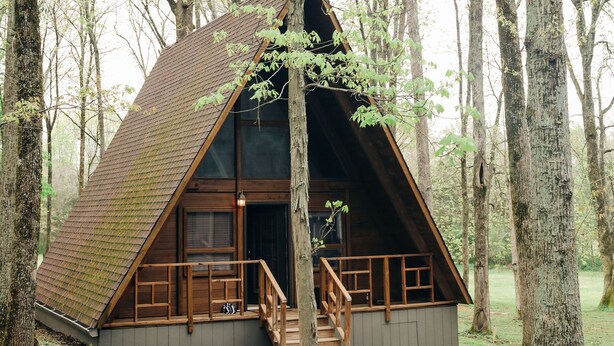 A wooden cabin with a triangular roof, surrounded by trees, and accessible by a wooden staircase. - Scenic, Full-Hookup Back-In Campsite Just Outside Nashville! (Mt. Juliet)