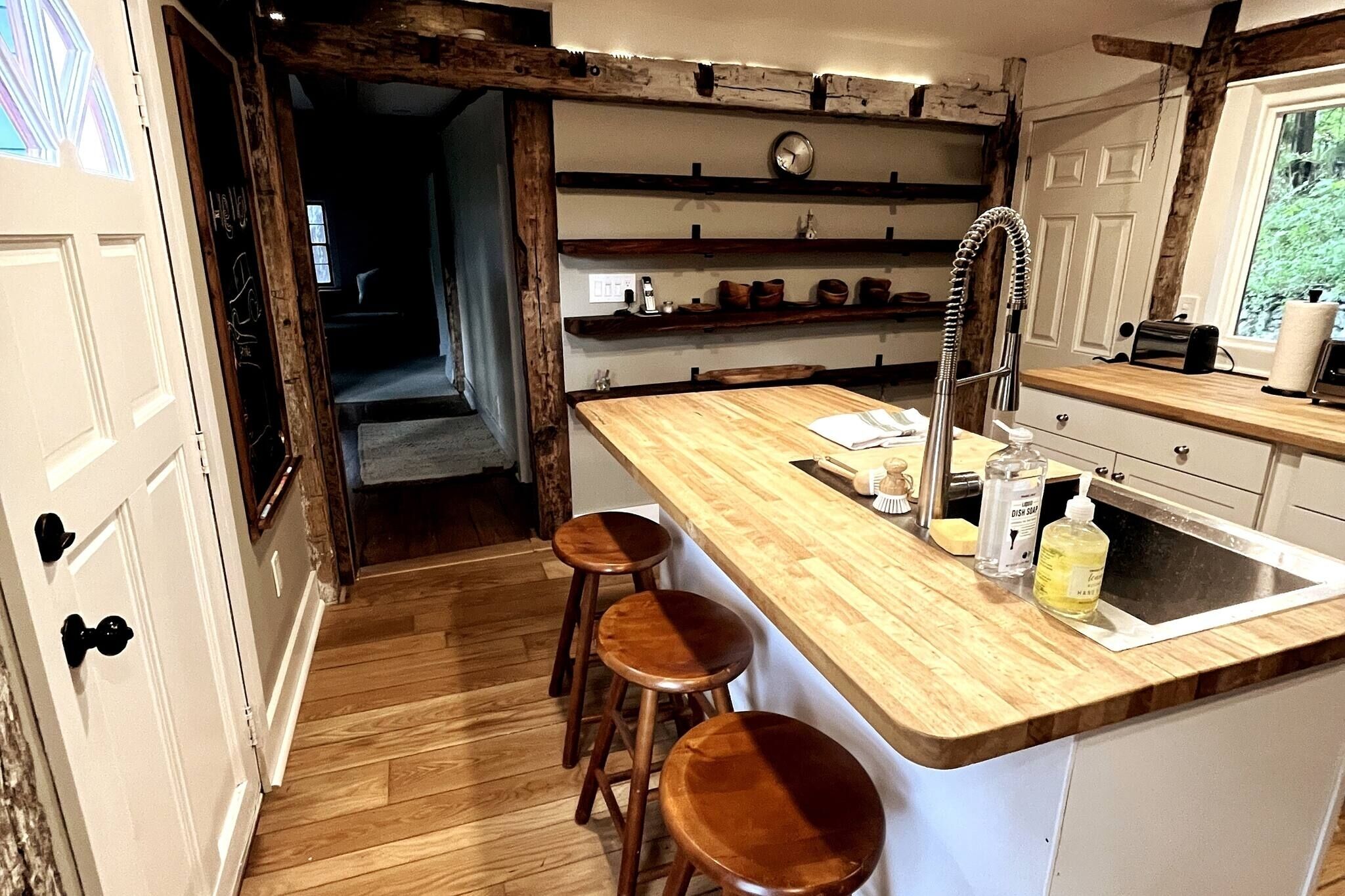 Une cuisine avec des tabourets en bois, un évier et des étagères remplies d’ustensiles de cuisine.