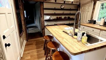 Une cuisine avec des tabourets en bois, un évier et des étagères remplies d’ustensiles de cuisine.