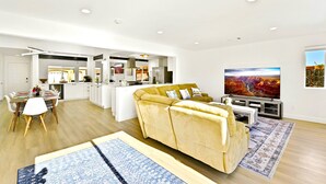 A modern living room with a sofa, a dining table, and a kitchen in the background. - Luxury Villa: Pool, Spa, Golf Views  Sleeps 12 (Indio)