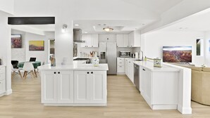 A modern kitchen with white cabinetry, a central island, and a dining area with a green table. - Luxury Villa: Pool, Spa, Golf Views  Sleeps 12 (Indio)