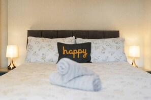 A neatly made bed with floral-patterned bedding and a pillow with the word 'happy' on it. - Unique Castle Stay in Perth - Corporate & Couples (Perth)