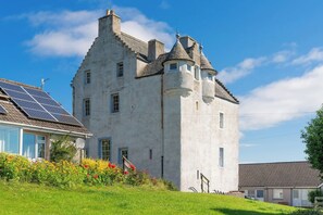 A castle-like building with a tower, surrounded by a well-maintained garden with colorful flowers.