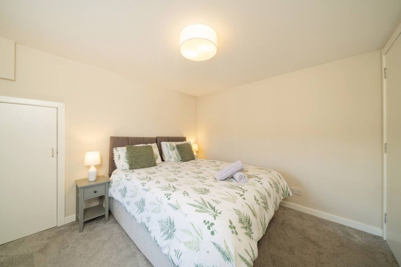 Une chambre à coucher avec un lit, une table de chevet, une lampe et une porte.