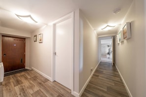 A hallway with wooden flooring, white walls, and a wooden door.