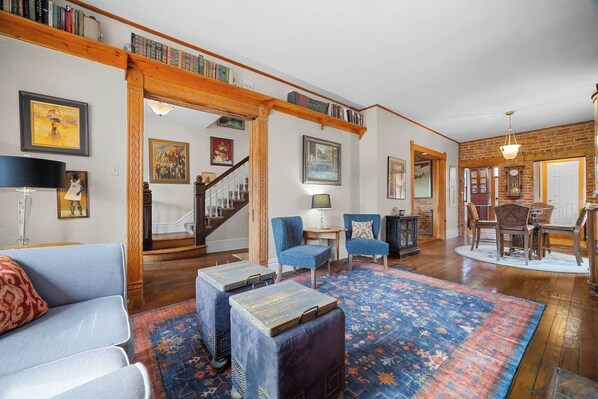 A spacious living room with a wooden staircase, a dining area, and a library.