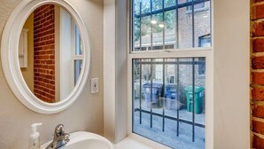 Une salle de bain avec un miroir rond, un lavabo blanc et une fenêtre donnant sur l’extérieur.
