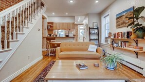 Un vaste espace de vie comprenant un canapé beige, une table basse et un escalier avec des balustrades blanches.