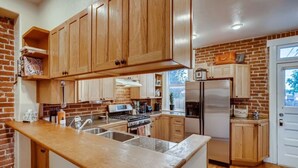 Une cuisine avec des meubles en bois, un réfrigérateur en acier inoxydable et un mur en briques.