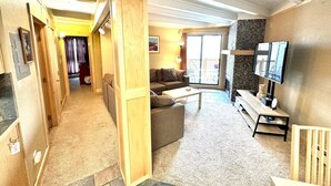 A spacious living room with a sofa, coffee table, and a TV. A wooden column divides the space, and there's a staircase leading to another level. - Fireplace I Pool I Biking I Skiing & Snowboarding (Silverthorne)