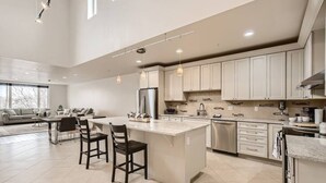 A modern kitchen with a central island, stainless steel appliances, and a dining area with a sofa and chairs. - Luxury Loft I Skyline Views in RiNO (Denver)