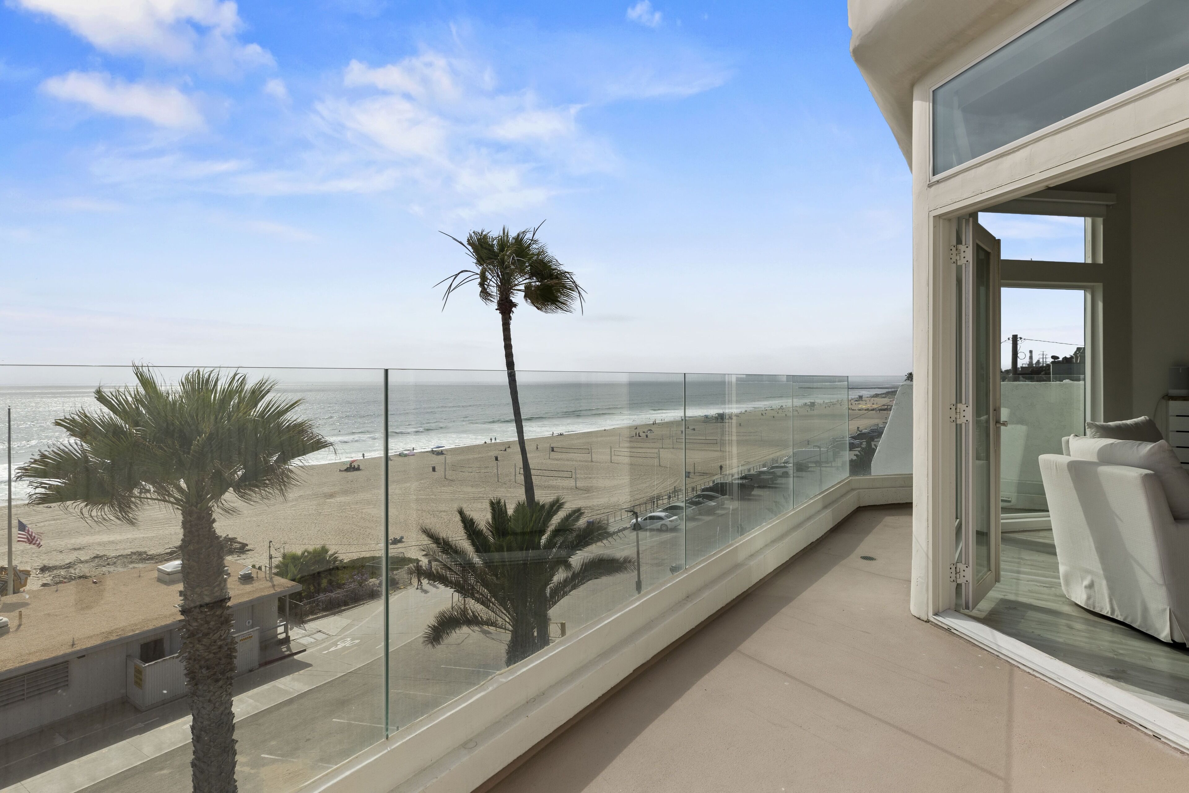 Un balcone con vista sulla spiaggia, palme e un cielo sereno.