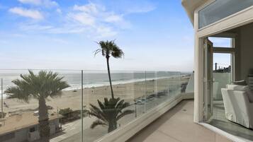 Un balcone con vista sulla spiaggia, palme e un cielo sereno.
