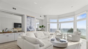 Una sala de estar moderna con un sofá blanco, una mesa de centro redonda y un ventanal con vista al océano.