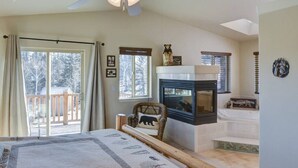 A bedroom with a large window, a ceiling fan, a fireplace, and a bed with a rug. - Cabin on 13 acres w/ Pool Table & Jacuzzi Tub! (Jefferson)