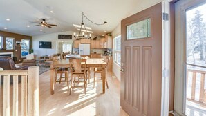 A spacious living area with a large wooden dining table, a ceiling fan, and a view of a snowy landscape through the sliding glass door. - Cabin on 13 acres w/ Pool Table & Jacuzzi Tub! (Jefferson)