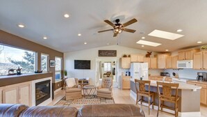 A spacious living room with a fireplace, a ceiling fan, and a large window overlooking a snowy landscape. - Cabin on 13 acres w/ Pool Table & Jacuzzi Tub! (Jefferson)