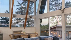 Uma sala de estar ampla, com um sofá modular grande, vigas de madeira e janelas amplas que oferecem vista para árvores.