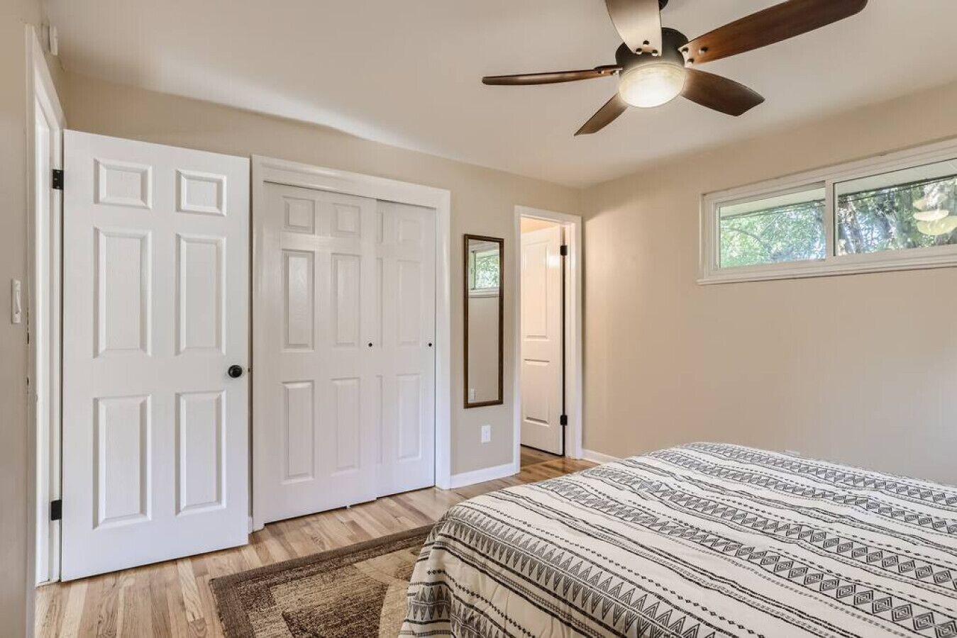 A bedroom with a bed, a ceiling fan, a window, and a door.