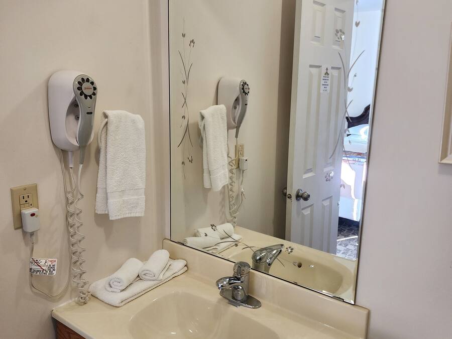 Uma casa de banho com lavatório, dois secadores de cabelo, espelho e um porta-toalhas.