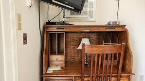 Ett skrivbord i trä med en tv, en lampa och en stol.