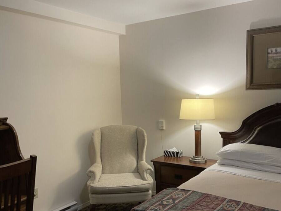 Habitació d'hotel amb un llit, una cadira, una tauleta de nit amb una làmpada i una catifes amb un disseny.