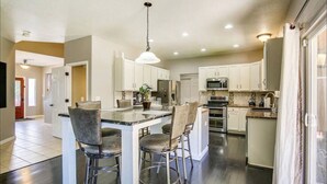 Una cocina moderna con armarios blancos, una isla central con taburetes de bar, electrodomésticos de acero inoxidable y una lámpara colgante.