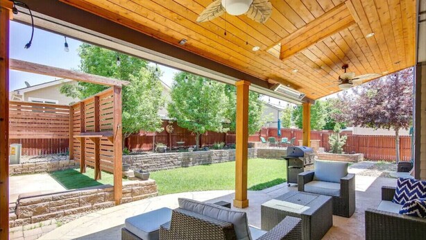 Un patio al aire libre con mobiliario de mimbre, una pérgola de madera y vistas a un jardín trasero.