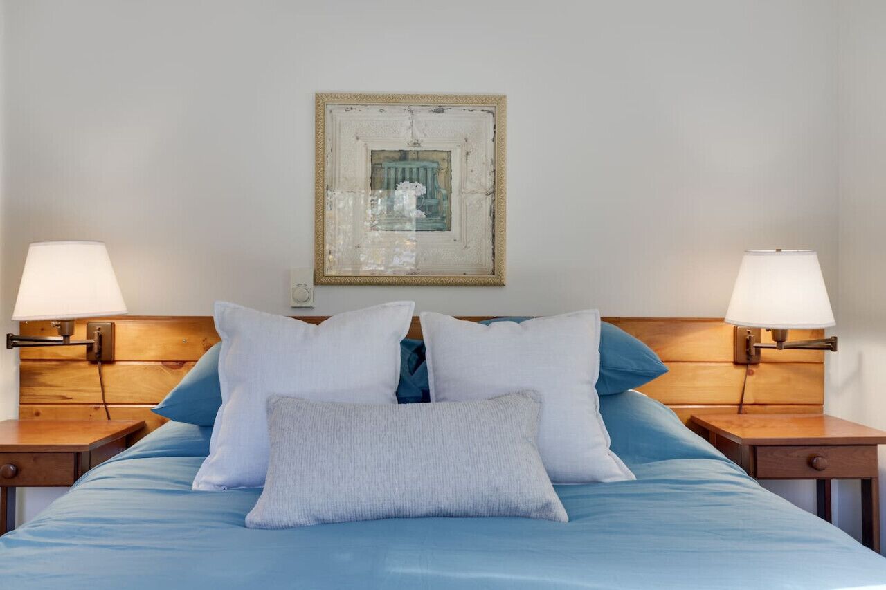 A neatly made bed with blue bedding, two bedside lamps, and a framed picture on the wall.
