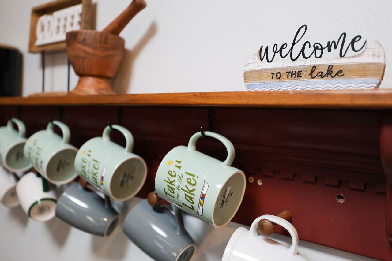 Un mur sur lequel est affiché un panneau indiquant « Bienvenue au bord du lac », et une rangée de tasses ornées de l’inscription « Emportez un peu de lac avec vous ».