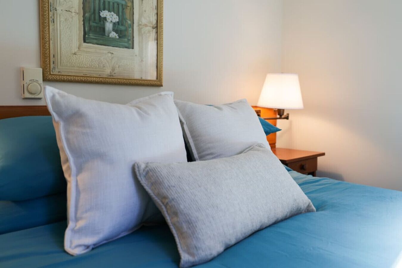 Una cama con dos almohadas y una mesita de noche con lámpara.
