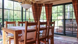 Ein Essbereich mit Holztisch und -stühlen, großen Fenstern mit Karottenvorhängen und einer Kristallleuchter.