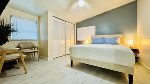 A bedroom with a large bed, bedside lamps, a chair, and a window with blinds.