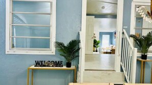 A hallway with a 'WELCOME' sign, a staircase, and a view into a living area with a sofa and plants.